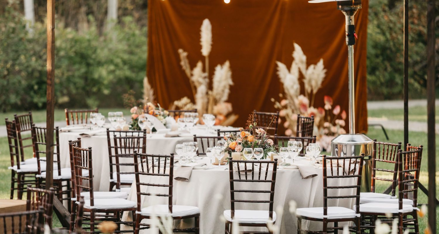 Wedding decor for newlyweds at banquet dried flowers, florist in boho style, catering service for bride and groom. Candles, accessories, glasses and plates on table, chairs for guests on green lawn