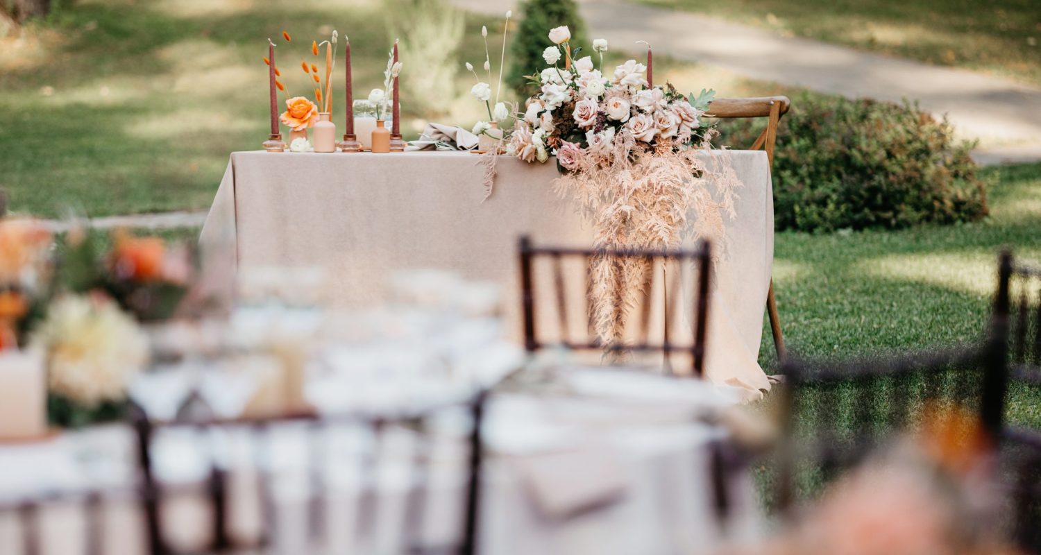 Place of newlyweds at party after wedding ceremony, nobody. View of table bride and groom with elegant bouquet with dry plants and serving, from guests seat on green lawn outdoor, flat lay, free space